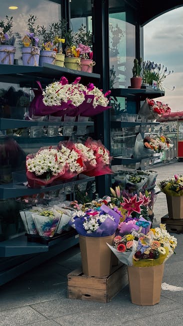 A display of fresh floral arrangements at North Harrow station, featuring bouquets of white, pink, and purple flowers wrapped in colorful paper and placed in cardboard boxes. The flowers include white